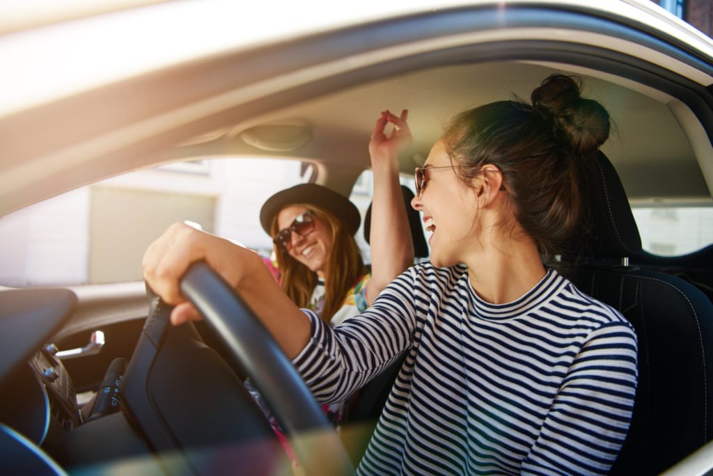 Two young women having fun driving along a street